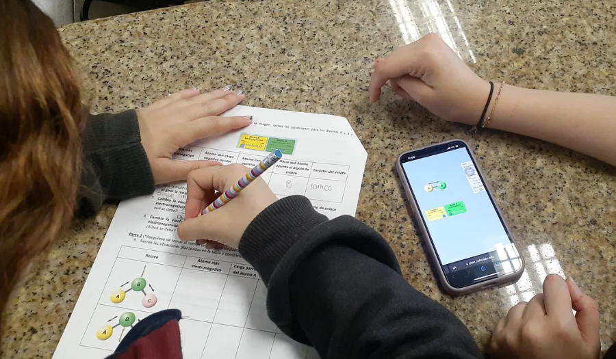 Two students interact with the Molecule Polarity simulation on a smartphone as one completes a worksheet.