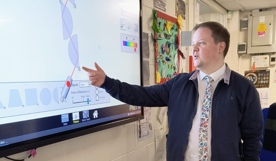 A teacher points to the Bending Light simulation on a smartboard as light rays reflect and refraction through lenses.