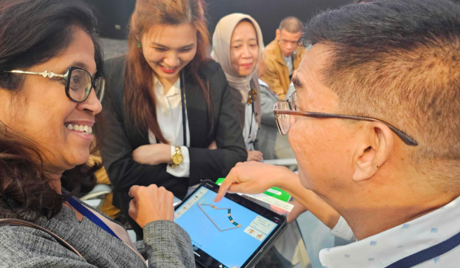 Four teachers converse and smile as they look at a tablet displaying the Circuit Construction Kit: DC simulation.