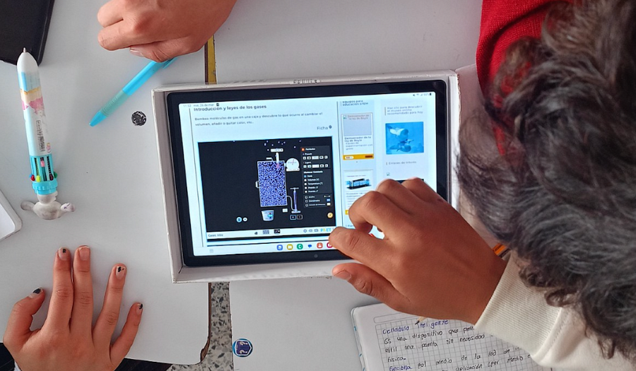 A group of students look toward the Gas Laws simulation on a tablet in the center of their desks.
